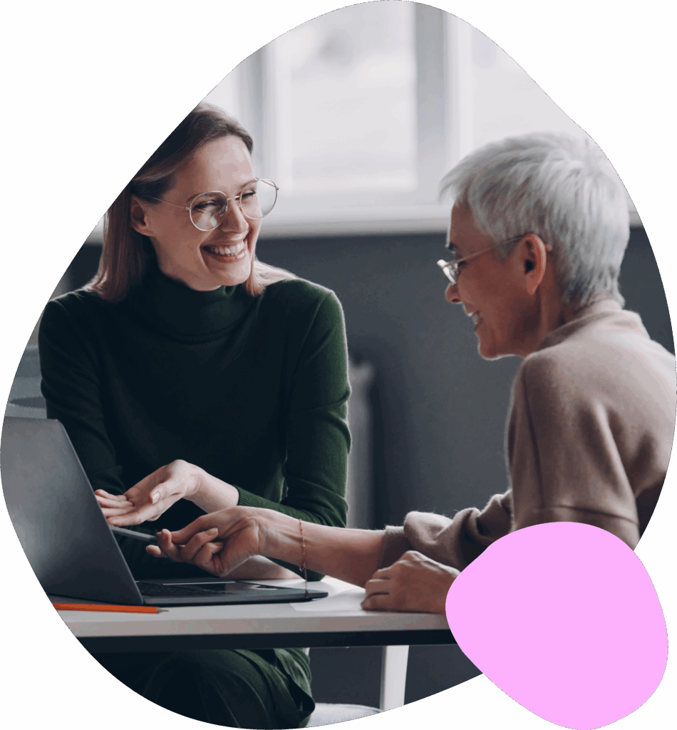 Two women at an office desk with one woman showing content on her laptop to the other woman